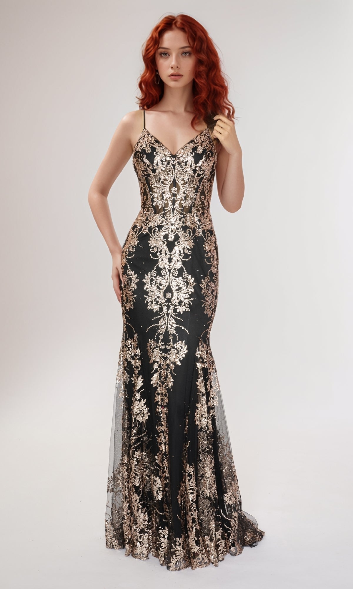 A woman with long red hair wears the Nina Canacci 1562, a black formal mermaid dress with gold floral embroidery, posing against a plain light background.